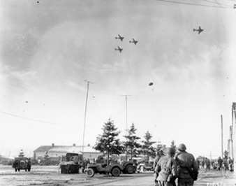Photo: SC415376 - BASTOGNE, BELGIUM Troops of the 101st Airborne Division watch C-47?s drop supplies to them. 26 December 1944.
